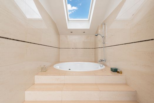 Contemporary bathroom interior with stairs and oval shaped bathtub under shower and cloudy blue sky in house