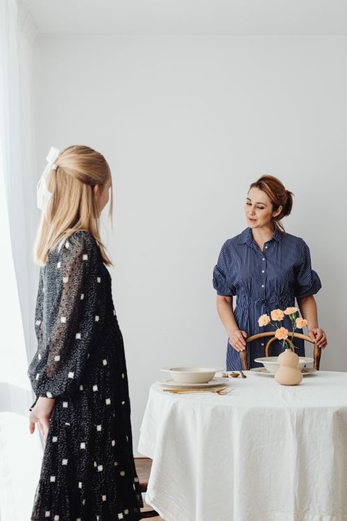 Free A mother and daughter setting up a dining table at home, with tableware and flowers. Stock Photo