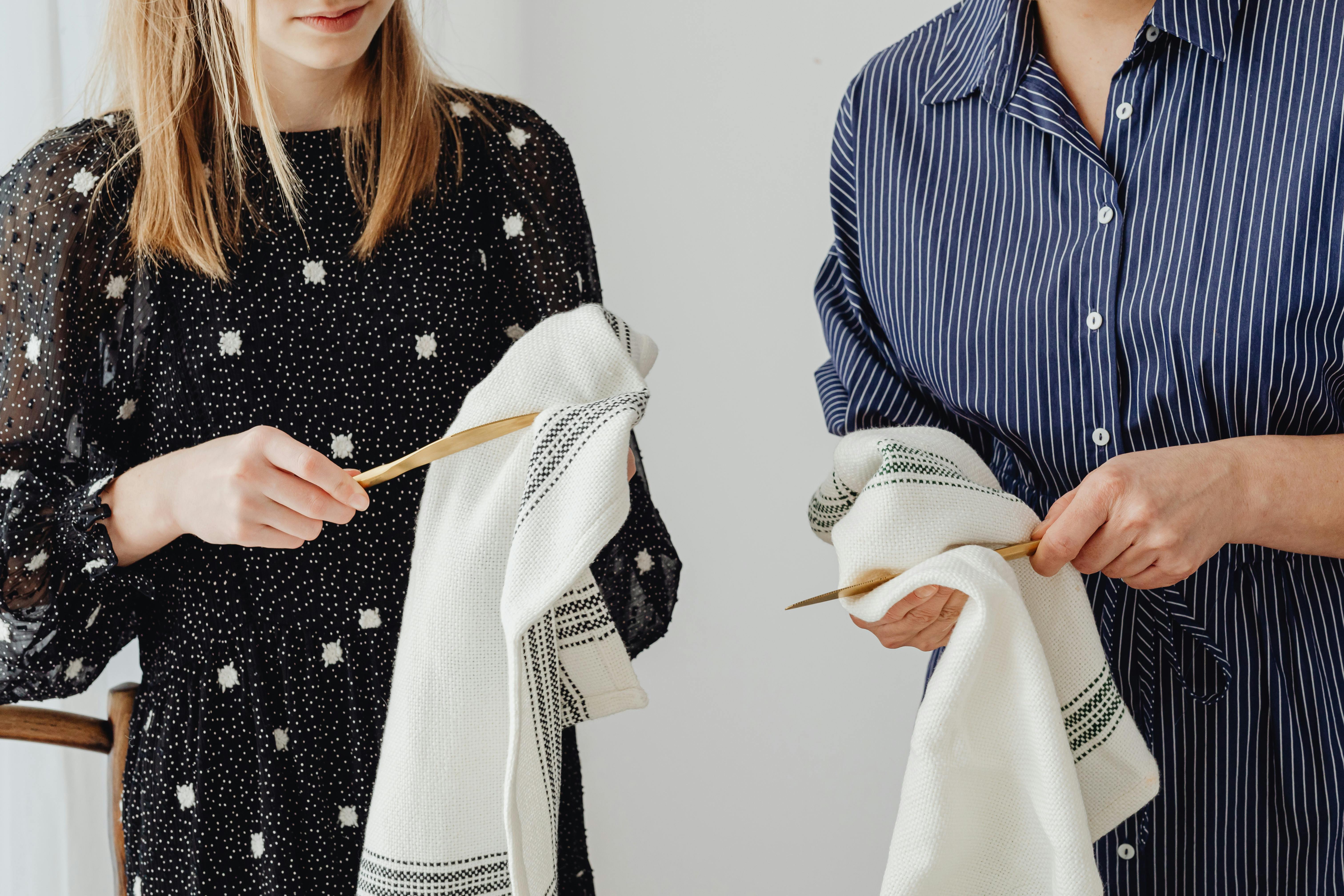 Close-up of two people drying dishes using white kitchen towels indoors.