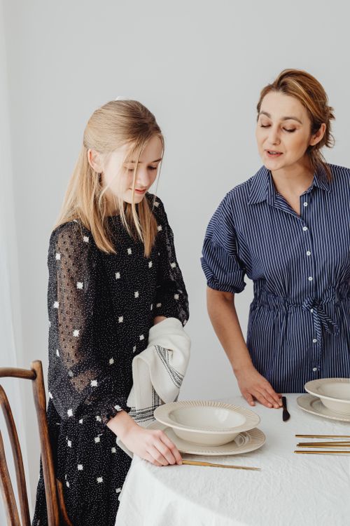 Free A mother instructs her daughter on table setting in a cozy dining area, fostering learning and family bonding. Stock Photo