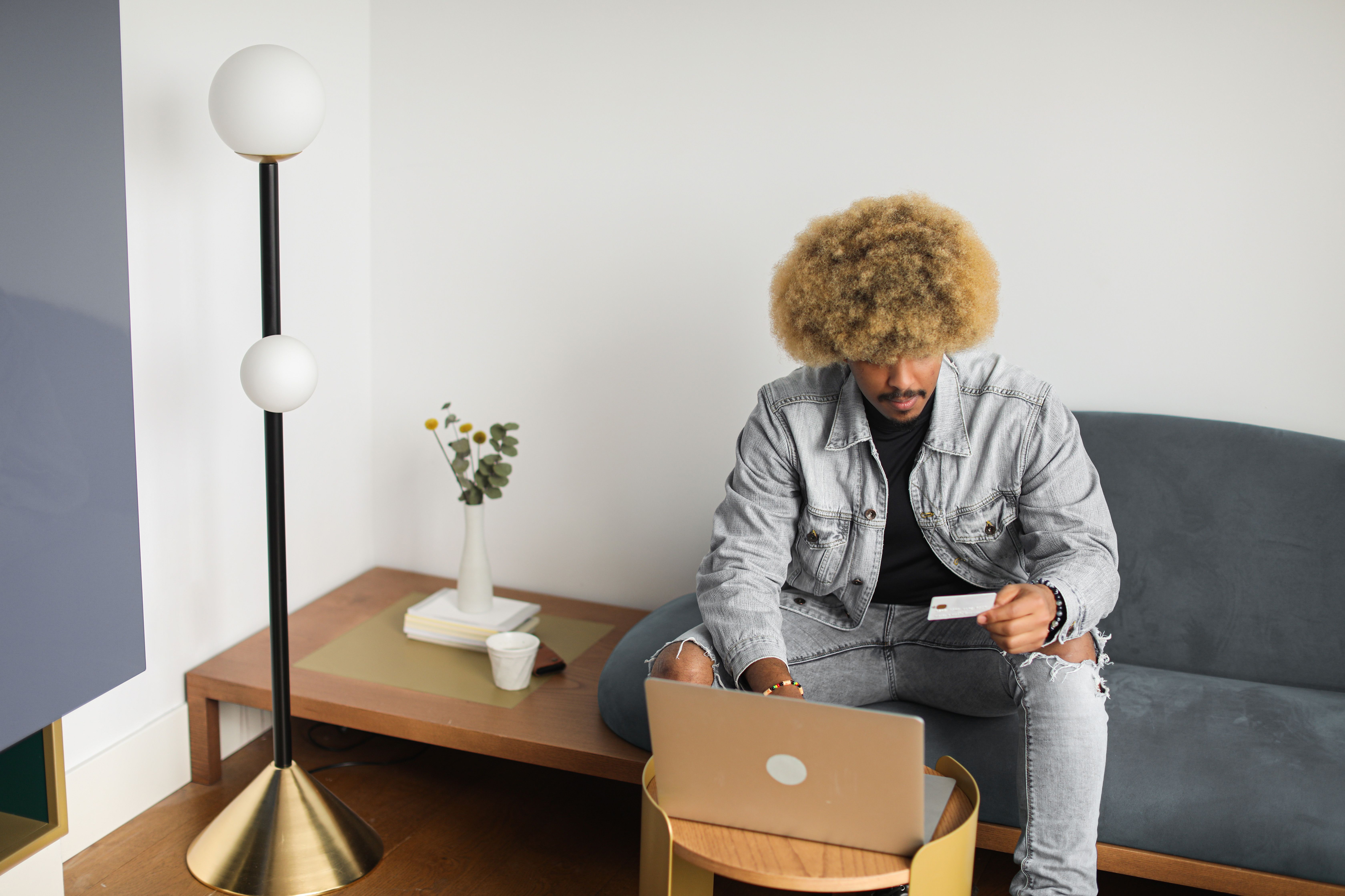 Stylish young man with afro hair uses a laptop and credit card for online shopping.