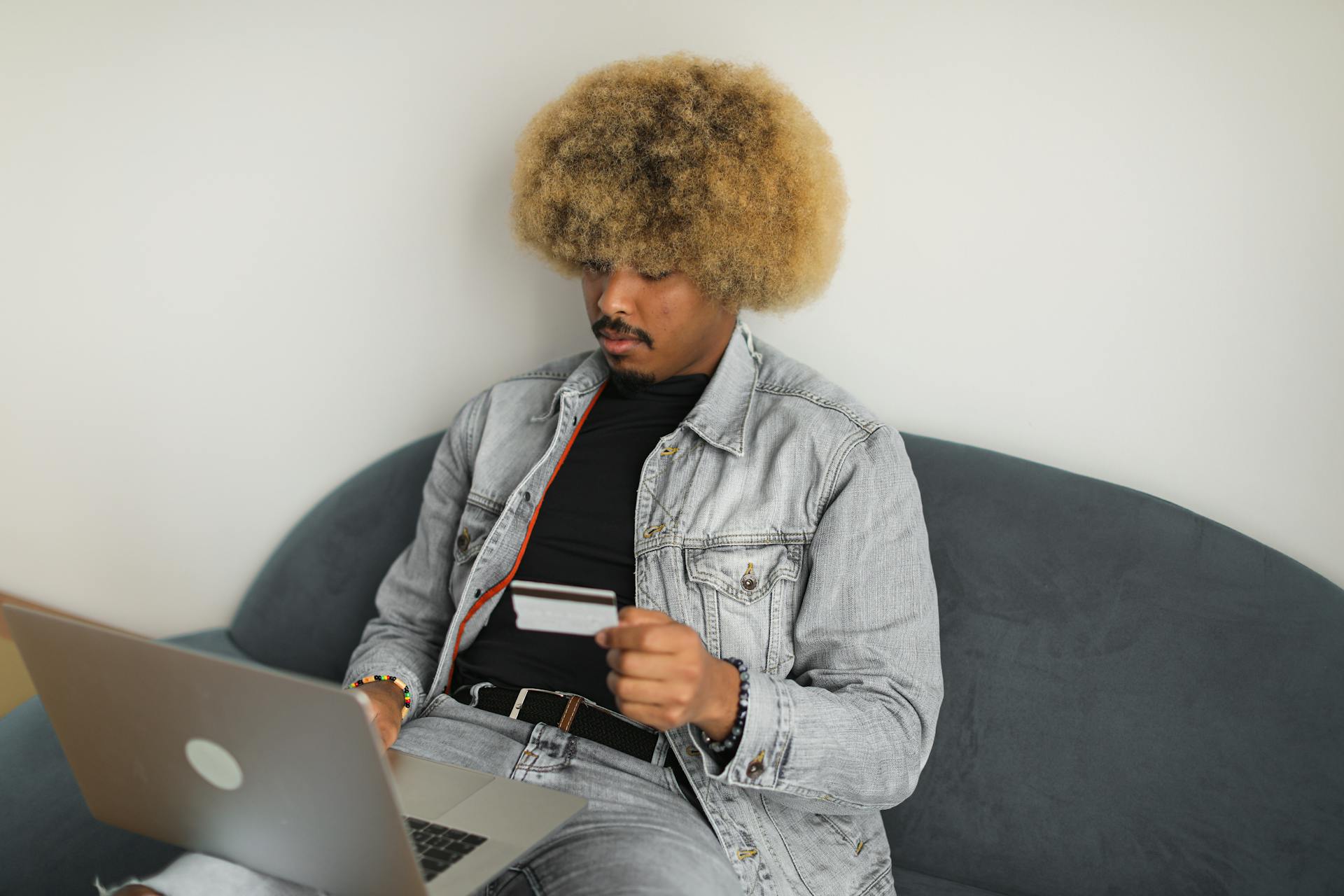 A man with afro hair using a credit card for online shopping while seated on a sofa.