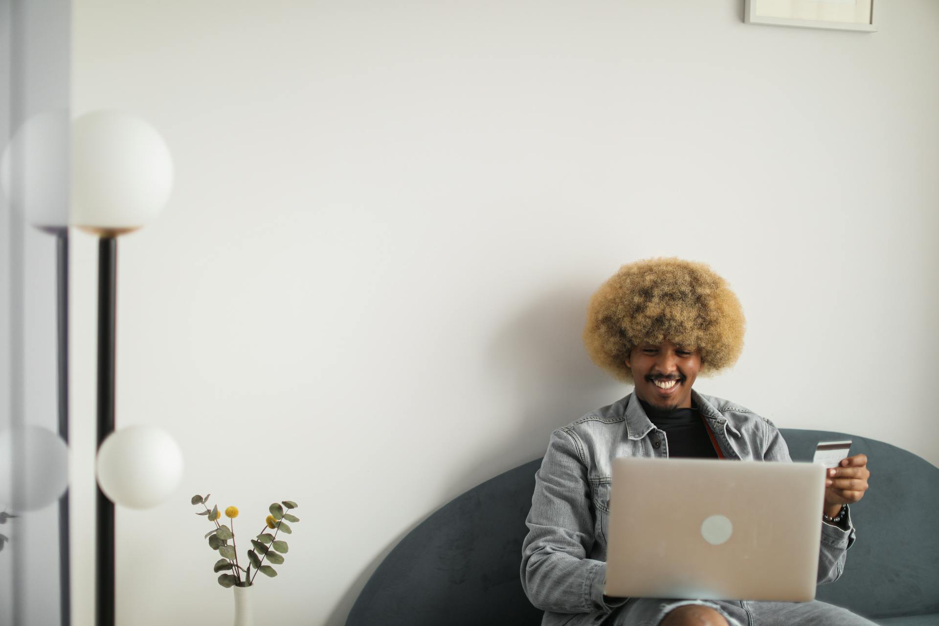 Smiling man in denim jacket using laptop and credit card for online shopping in cozy room.