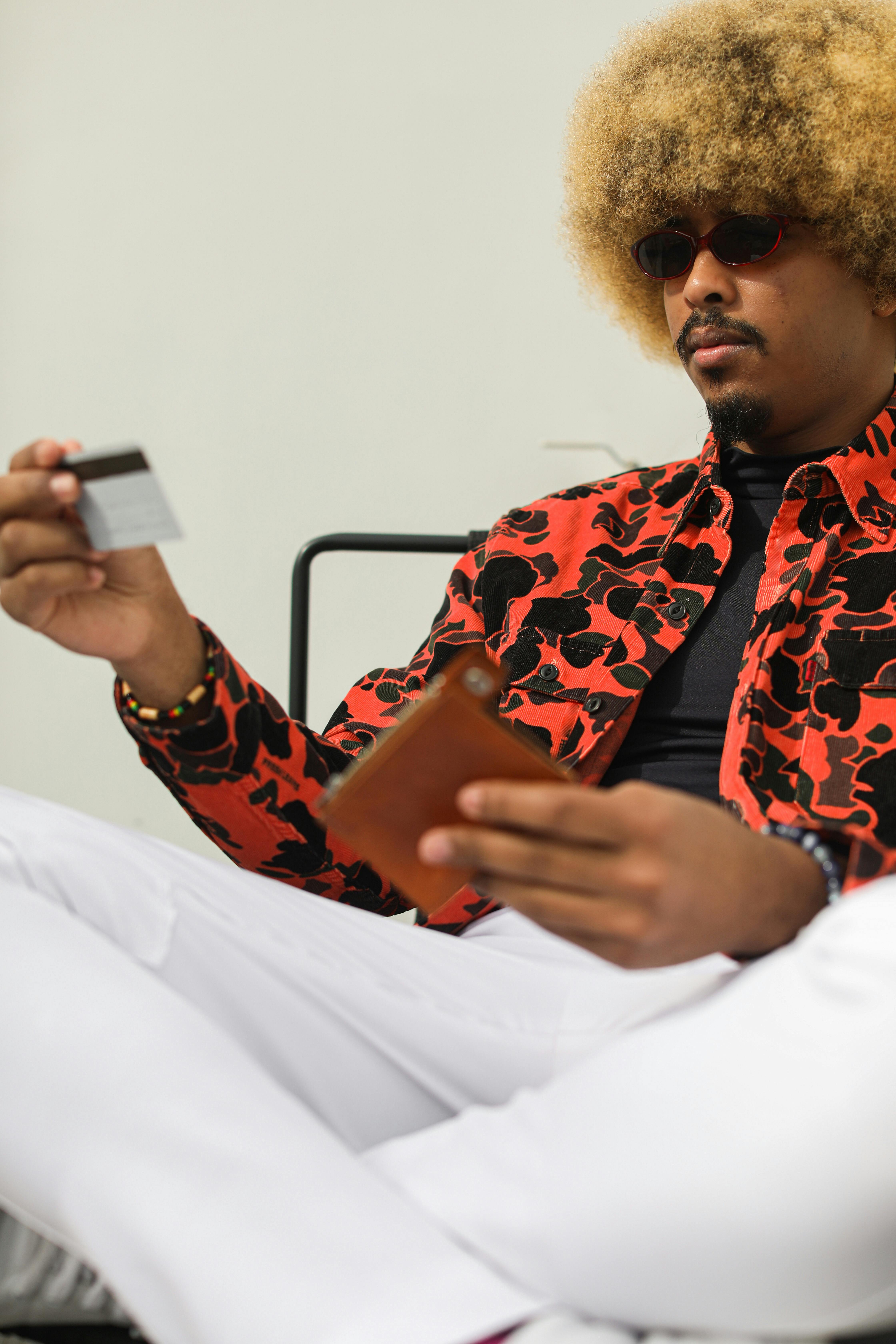 Stylish man with afro and sunglasses holding a credit card, engaged in online shopping.