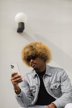 African American man in denim jacket using smartphone outdoors under modern lighting.