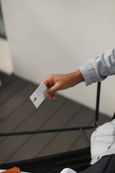 A person's hand holding a white credit card indoors, ready for an online purchase.