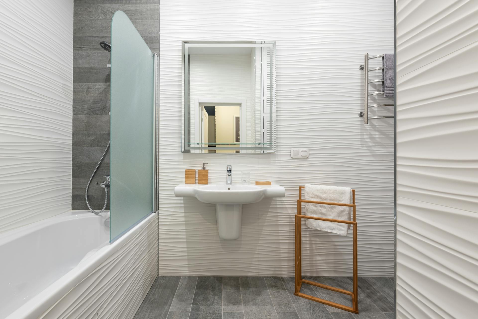 Contemporary bathroom interior with bathtub and washstand with toiletry products under mirror in light house