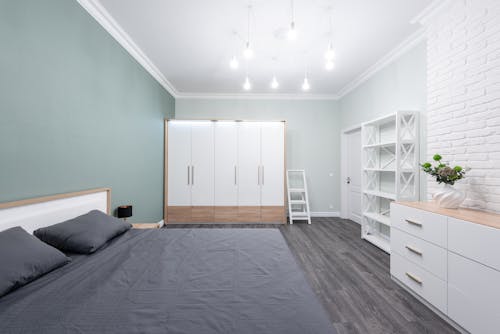 Bed with pillows and crumpled cover against closet and commode illuminated by light bulbs in modern house