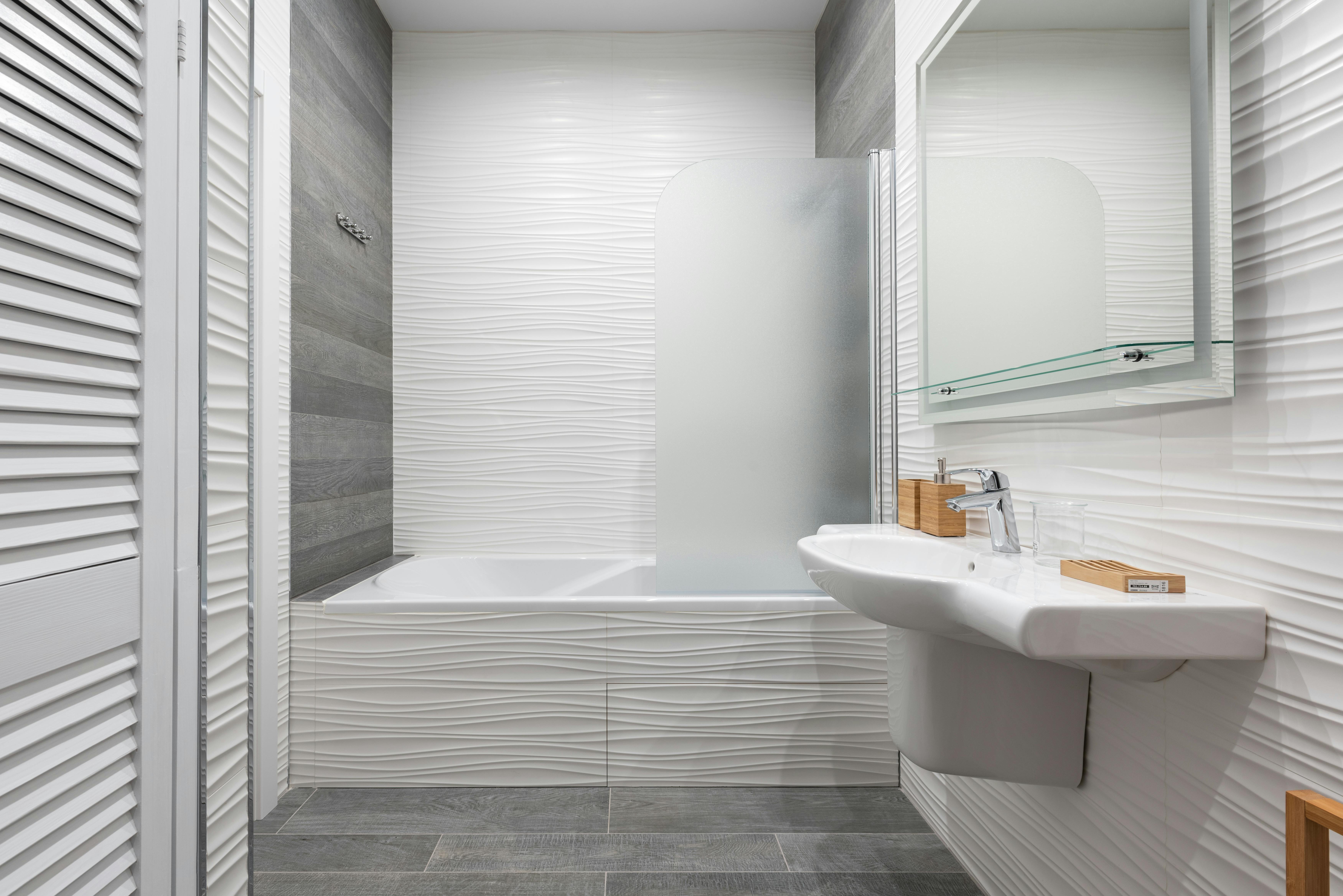 A white bathroom where lighting highlights a textured tile wall - White bathroom lighting
