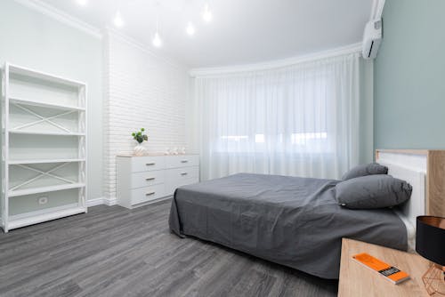 Minimalist interior of cozy bedroom with white furniture and curtains