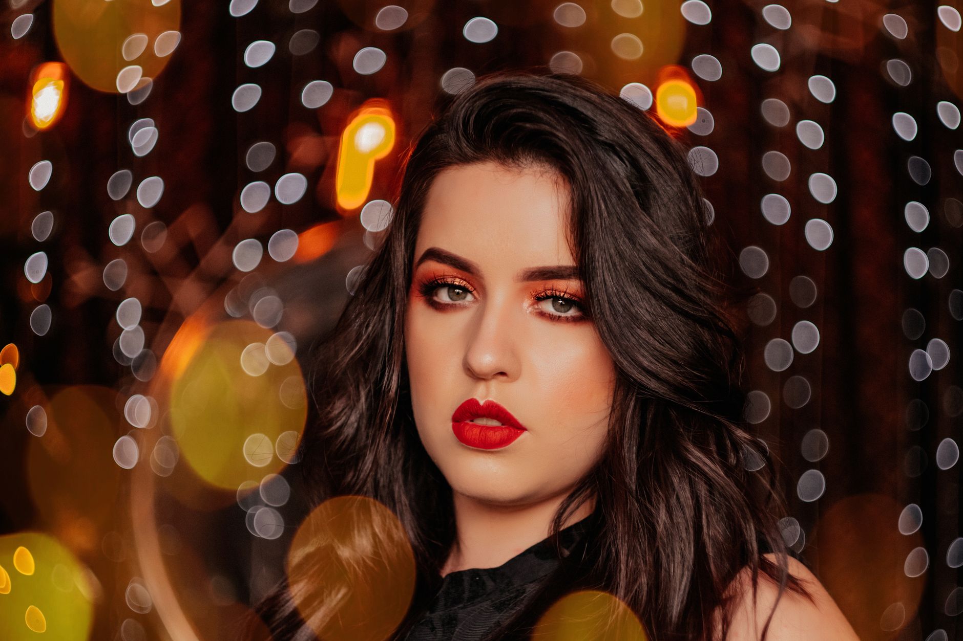 Elegant close-up of a woman with bold makeup in a bokeh lights setting.