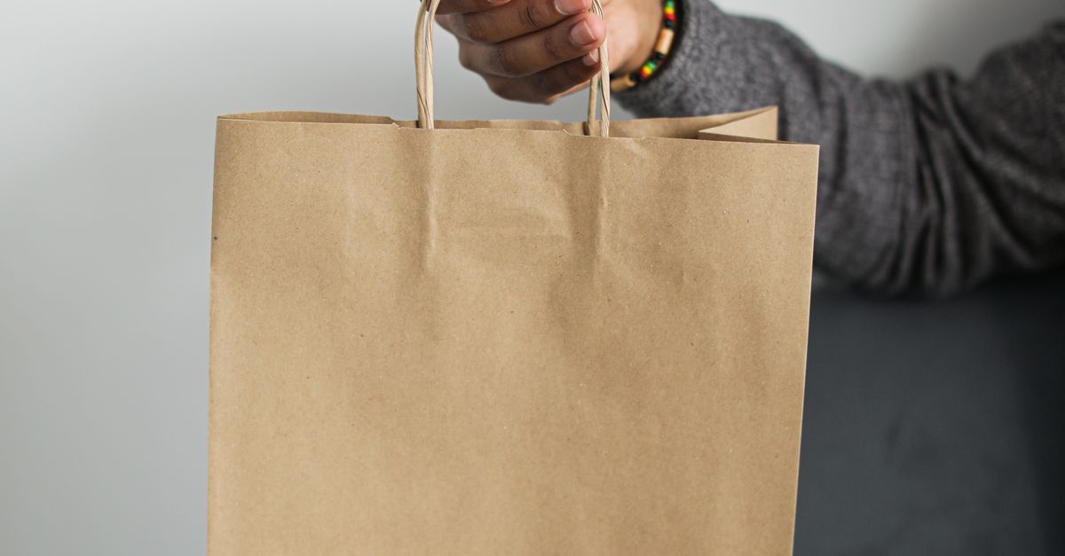 Close-up of a hand holding a brown paper shopping bag, emphasizing eco-friendly retail packaging.