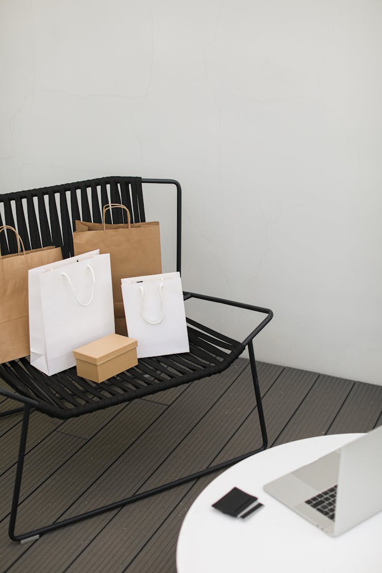 Shopping Bags On Black Chair Near A Table With Laptop And Bank Card