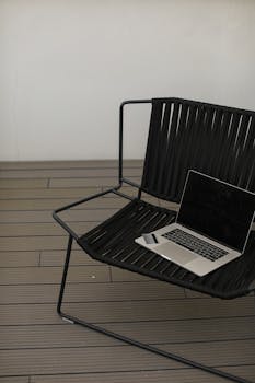 A sleek laptop rests on a black patio chair set on a wooden deck, evoking remote work vibes.
