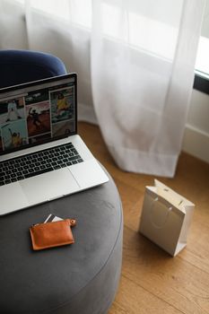 Photo of a laptop displaying images next to a wallet and shopping bag, indoors.