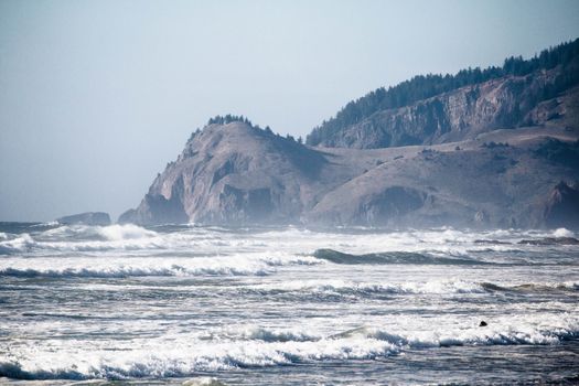 Dramatic ocean waves crashing against Oregon's rugged cliffs under a clear sky.