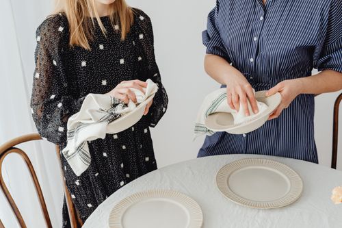 Free Women drying ceramic bowls and setting a table with plates and napkins. Stock Photo