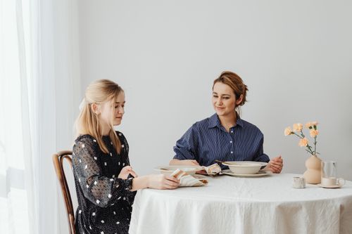 Free A mother and daughter sit at a table with flowers, enjoying dinner in a cozy indoor setting. Stock Photo