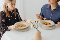 Two women enjoying homemade pumpkin soup at a dining table with floral decor.