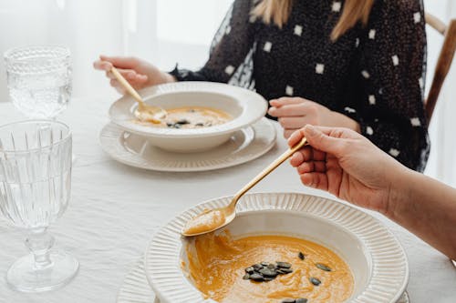 People Holding a Gold Spoon while Getting Soup from the Bowl
