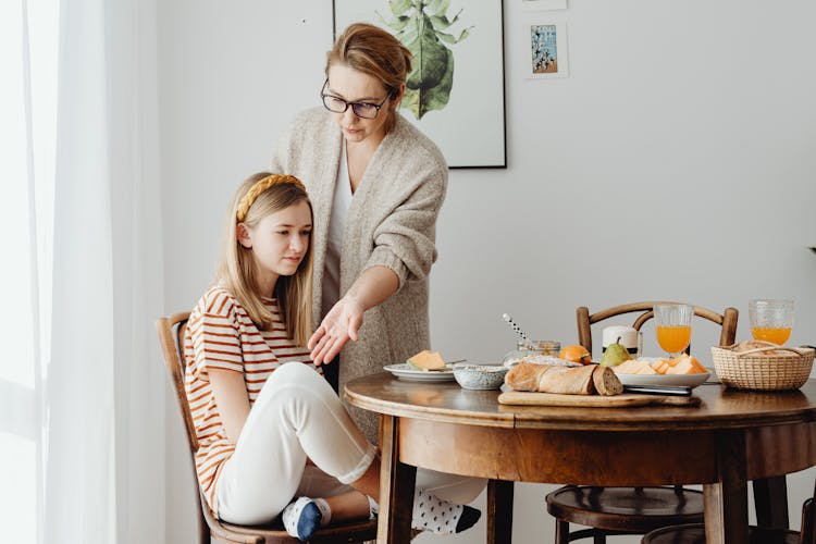 A Woman In Eyeglasses Teaching A Young Girl How To Sit Properly