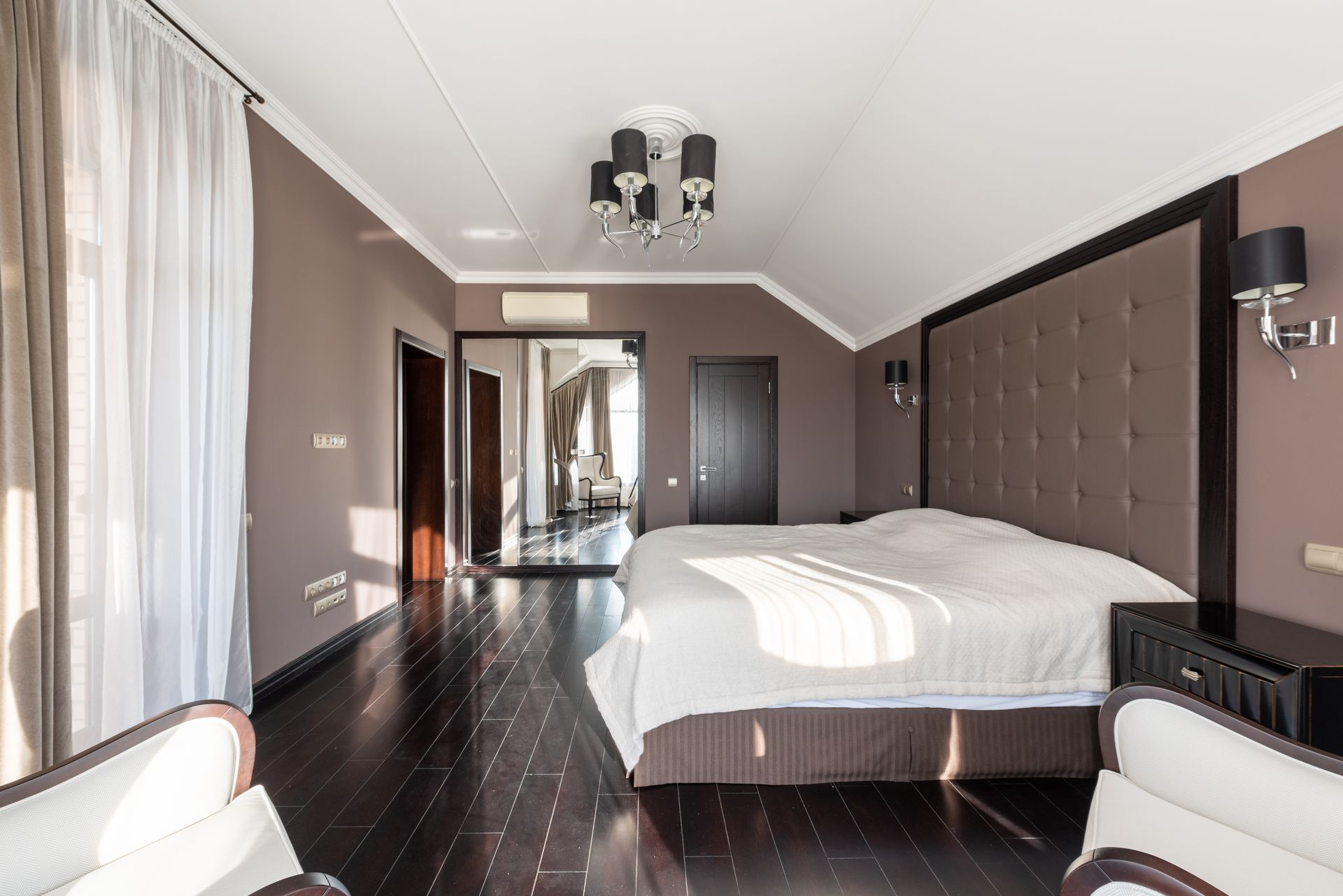 Comfortable bed with white blanket placed at wall with lamps in stylish light bedroom with doors and mirror at home