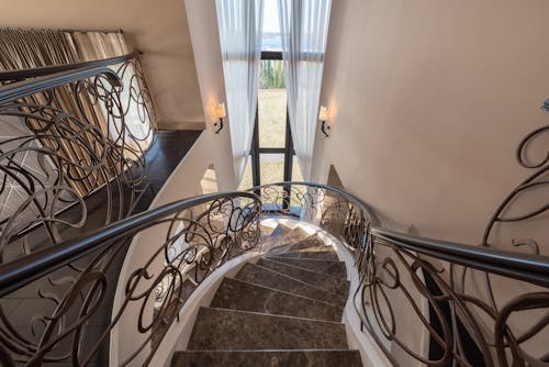 From above of stairway with marble steps and metal railings with ornamental elements located near window with tulle in contemporary building
