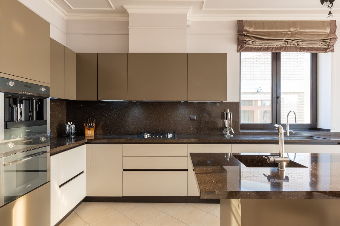 Free Table With Tap Placed In Modern Spacious Kitchen With Window And Brown Cupboards And Contemporary Appliances And Various Utensils At Home Stock Photo