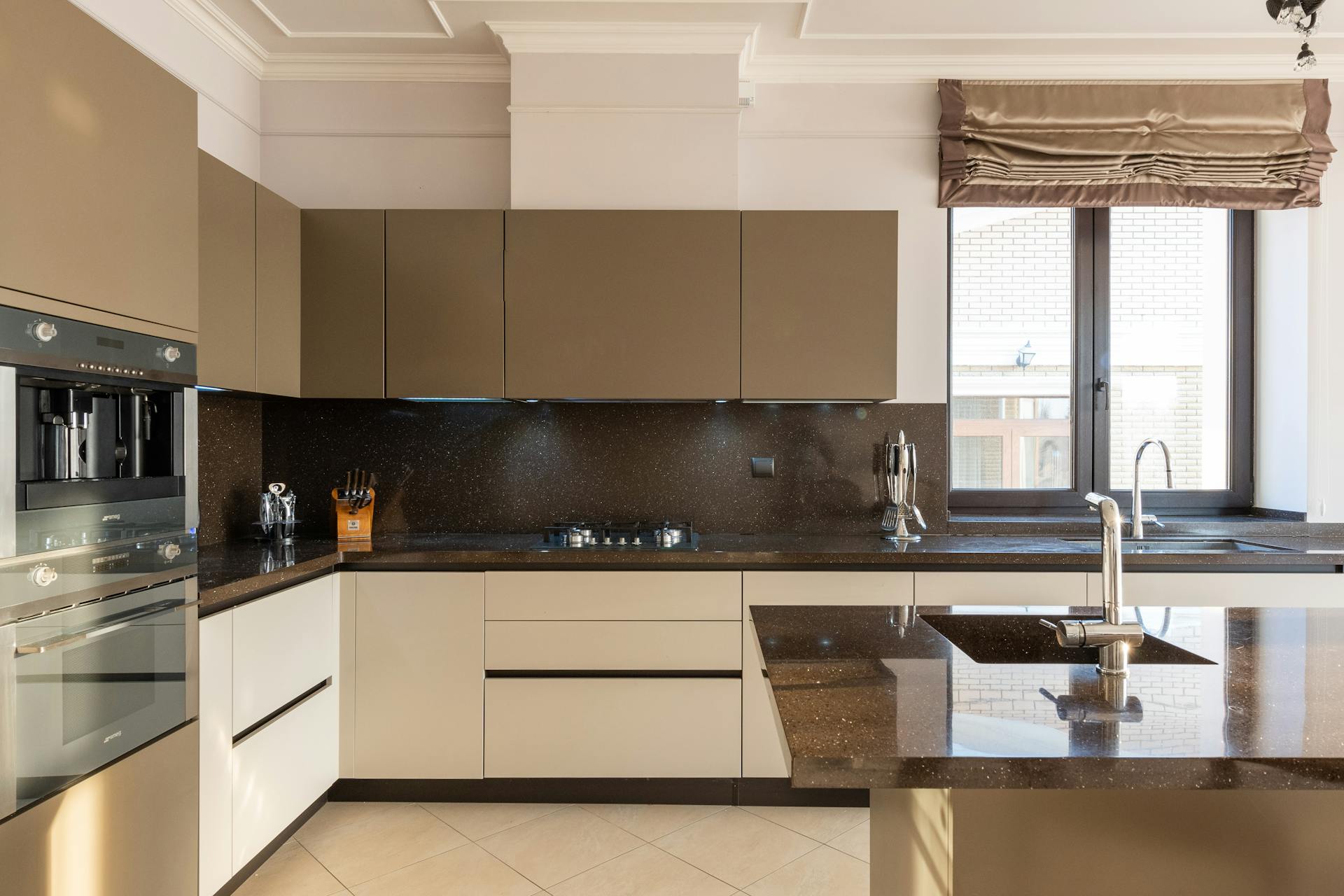 Table with tap placed in modern spacious kitchen with window and brown cupboards and contemporary appliances and various utensils at home