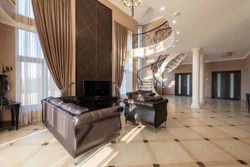 Free Soft leather black couches on tiled floor near window with curtains in modern stylish house with stairway and doors near columns Stock Photo