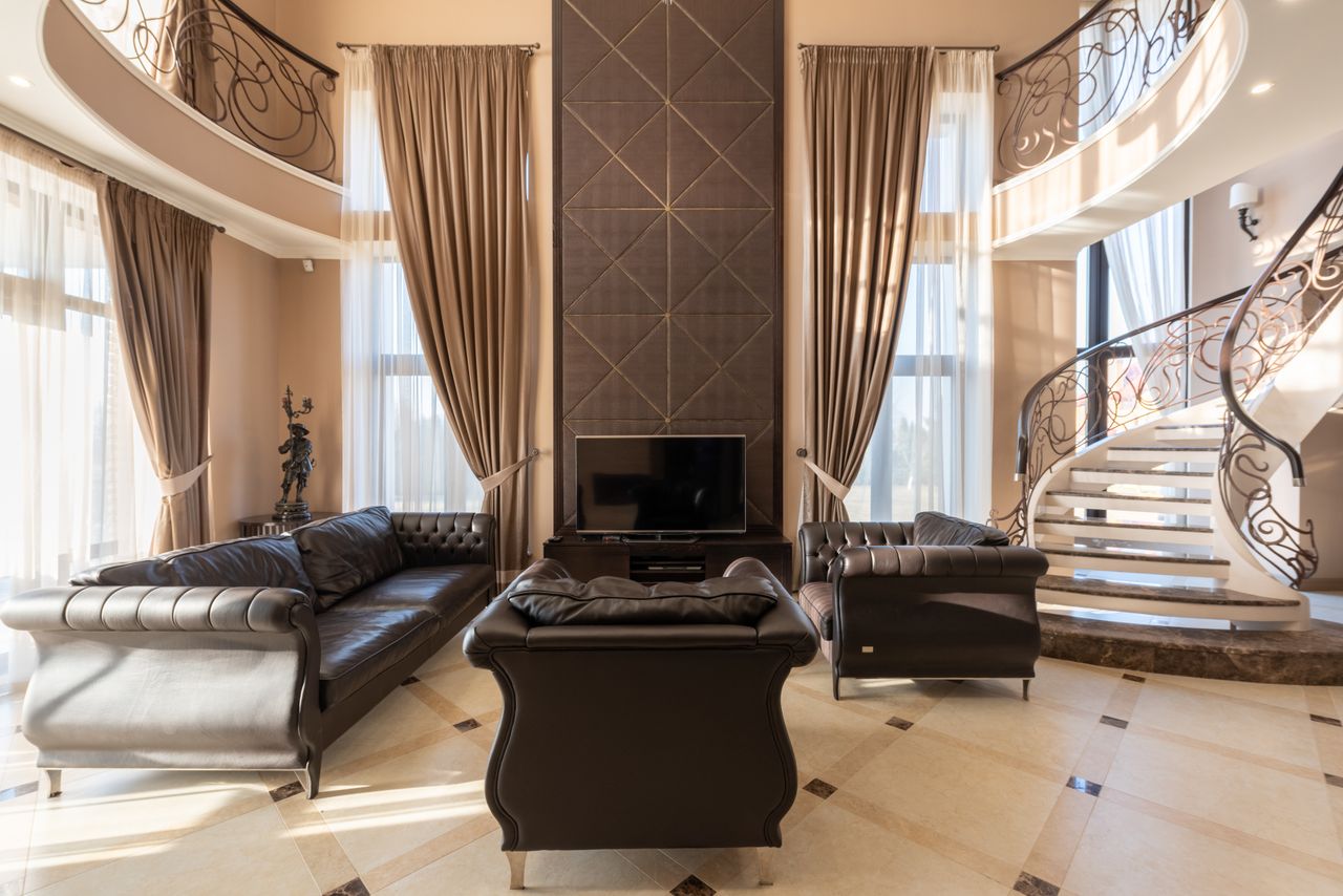 Two-story living room with floor-to-ceiling taupe drapes, sheer panels, and a curved staircase
