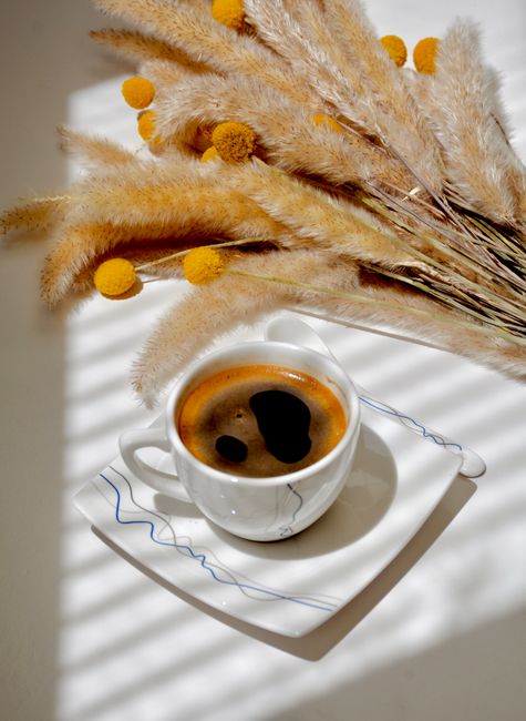 From above of cup of fresh hot coffee placed on table near yellow craspedia flowers in room with bright sunlight