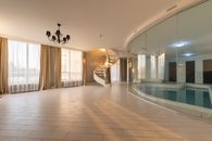 Swimming pool with clear water behind glass wall placed in modern hall with stairway and windows with curtains in contemporary house