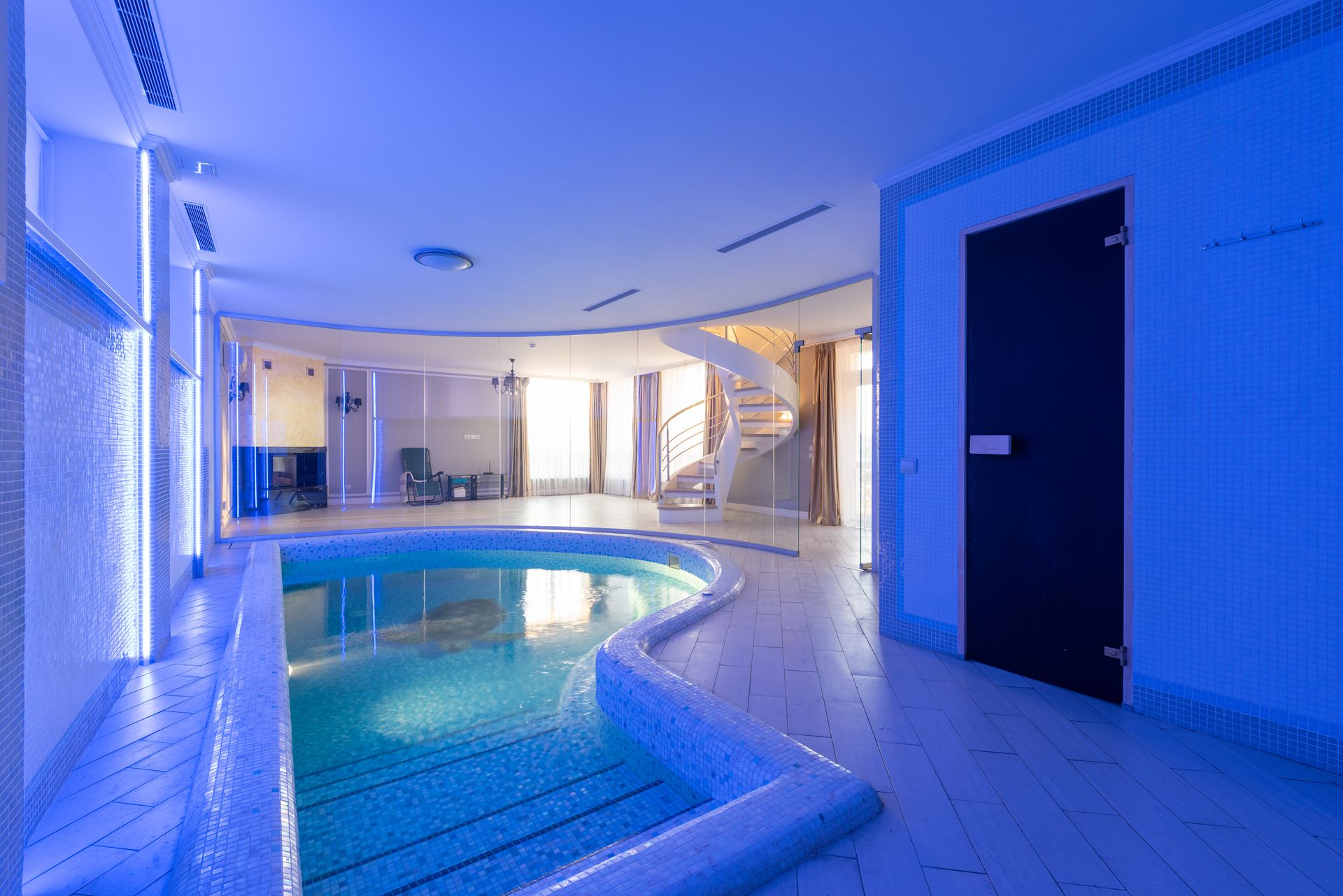Swimming pool with clear water placed in spacious room at wall with blue illumination and staircase in contemporary luxury house
