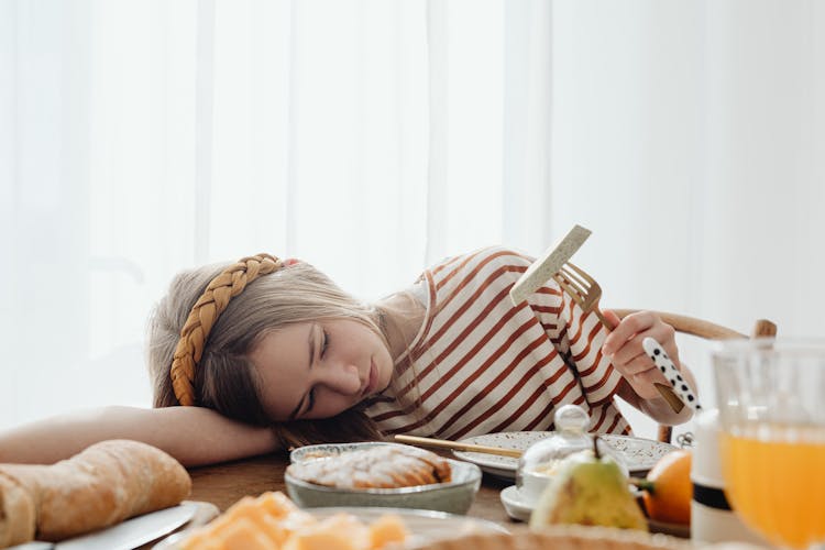 A Girl Lying On The Table While Holding A Fork