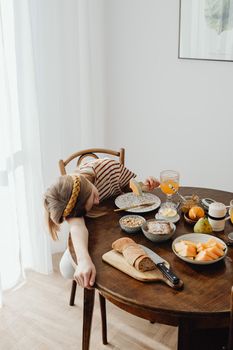 A teenager naps at a breakfast table filled with various foods and drinks on a sunny morning.