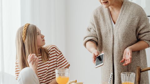 Two women enjoy a casual breakfast at home, chatting and sharing food.