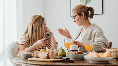 A mother and daughter engage in a conversation over breakfast, with an array of food on the table.