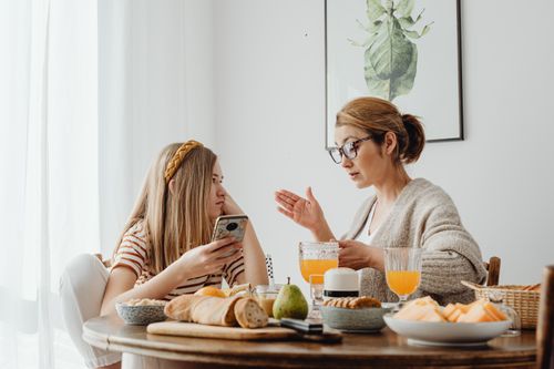 Free Mother and daughter enjoying breakfast with fresh juice and pastries at home. Stock Photo