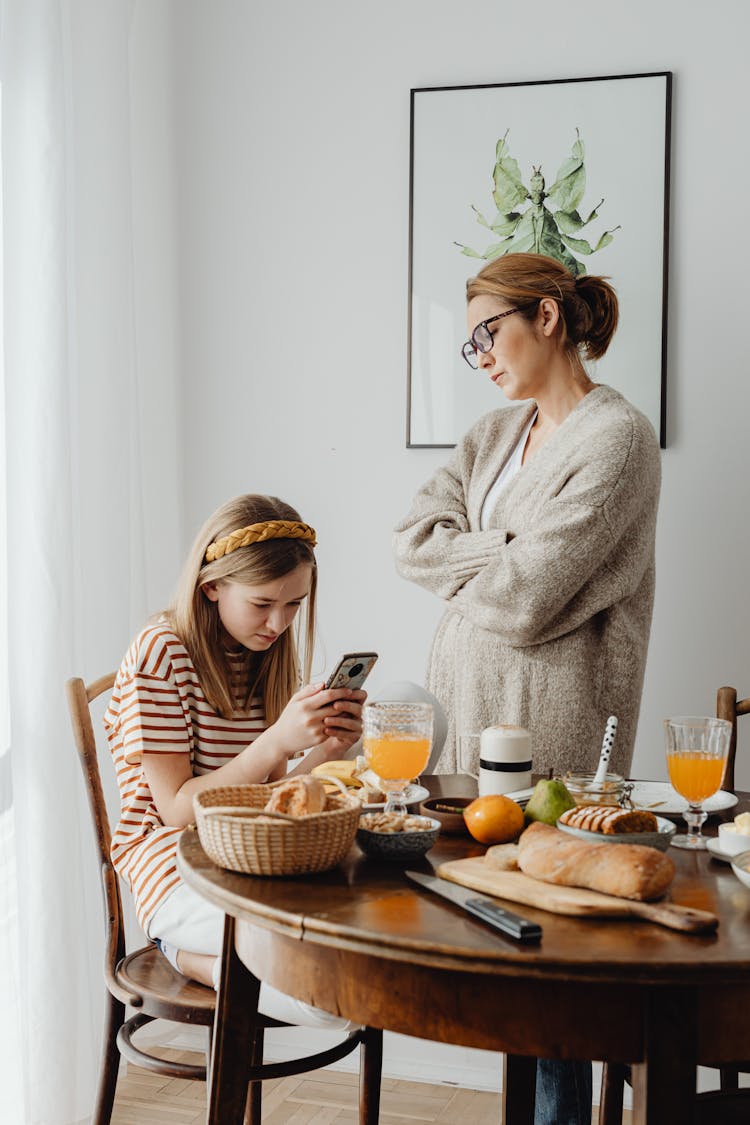 A Woman Looking Mad To A Young Girl While Using Her Smartphone