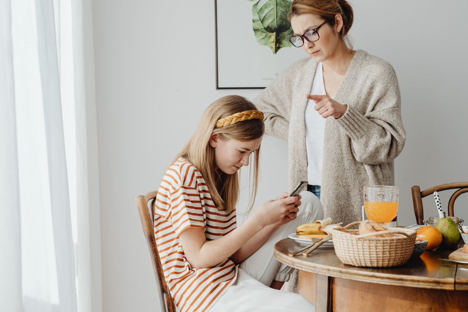 A mother scolds her teenage daughter for using a cellphone during breakfast at the dining table.