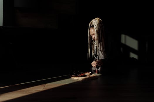 A woman with braided hair arranges a tray of sliced fruits in dim lighting, creating a serene ambiance.