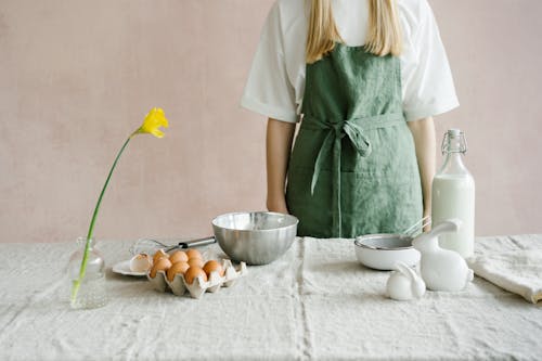 A person in a green apron preparing for Easter baking with eggs and milk indoors.