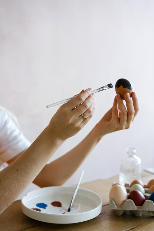 Free Close-up of hands skillfully painting an Easter egg with a brush. Stock Photo