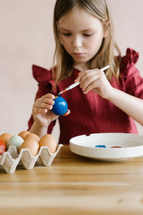 Free A young girl decorates Easter eggs with paintbrush at home. Stock Photo