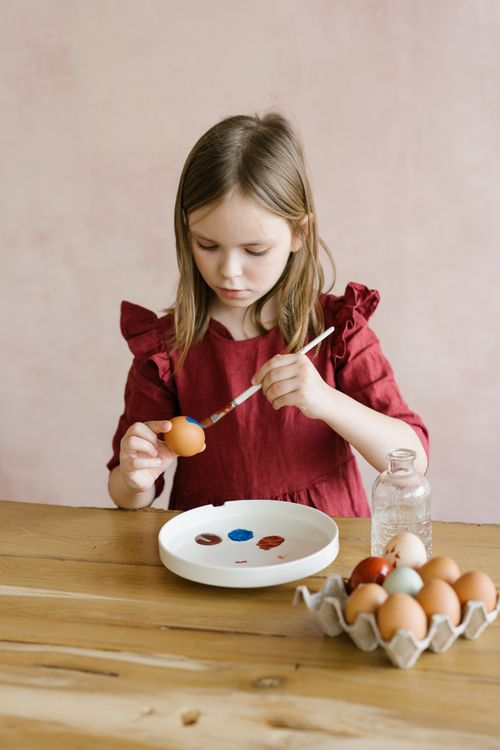 Free A young girl focused on painting Easter eggs with creative flair in an indoor setting. Stock Photo