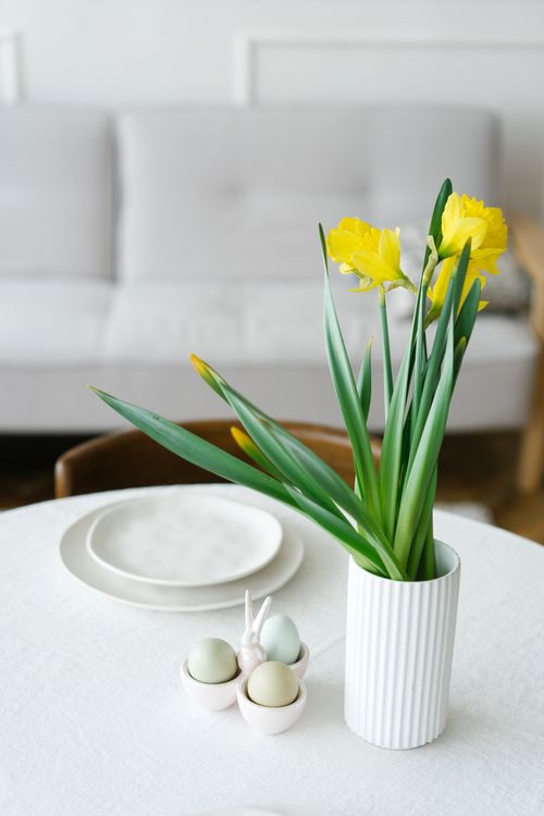 Free Easter table setup featuring vibrant yellow daffodils in a vase and pastel eggs for festive decor. Stock Photo