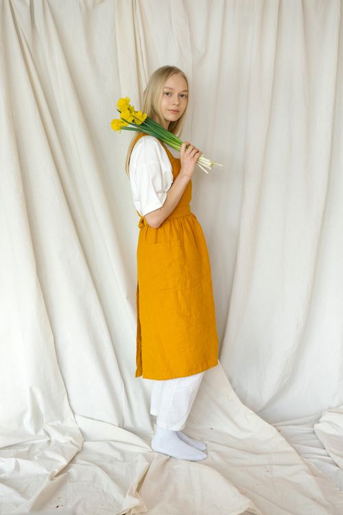 Free A teenage girl in a yellow apron holding yellow flowers in an indoor studio setting. Stock Photo