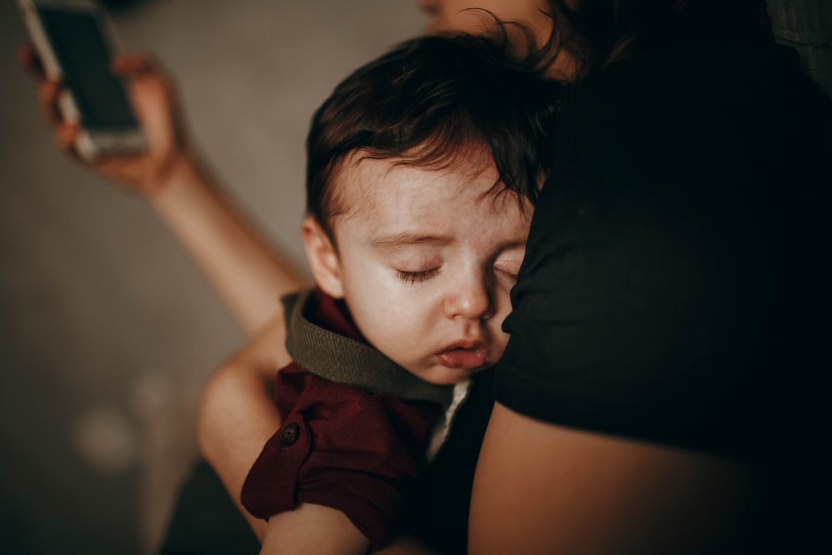 Tired mother holding her sleeping baby while scrolling her phone during a night feed, wondering when baby sleep gets better
