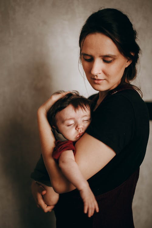 Caring mother with cute little son napping in arms standing near wall in light room during bed time at home